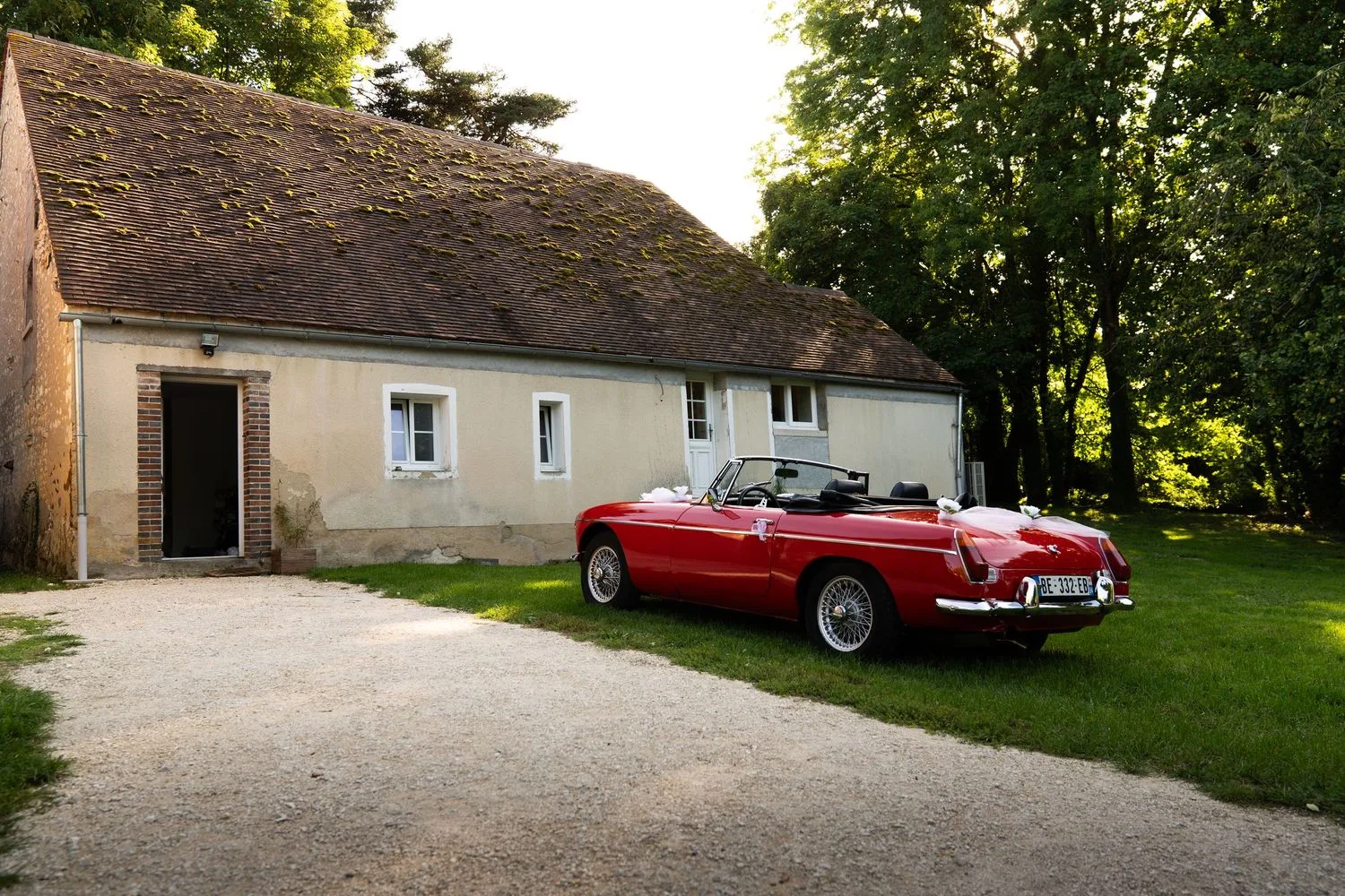 Voiture de mariage décorée de rubans blancs devant une dépendance en pierre