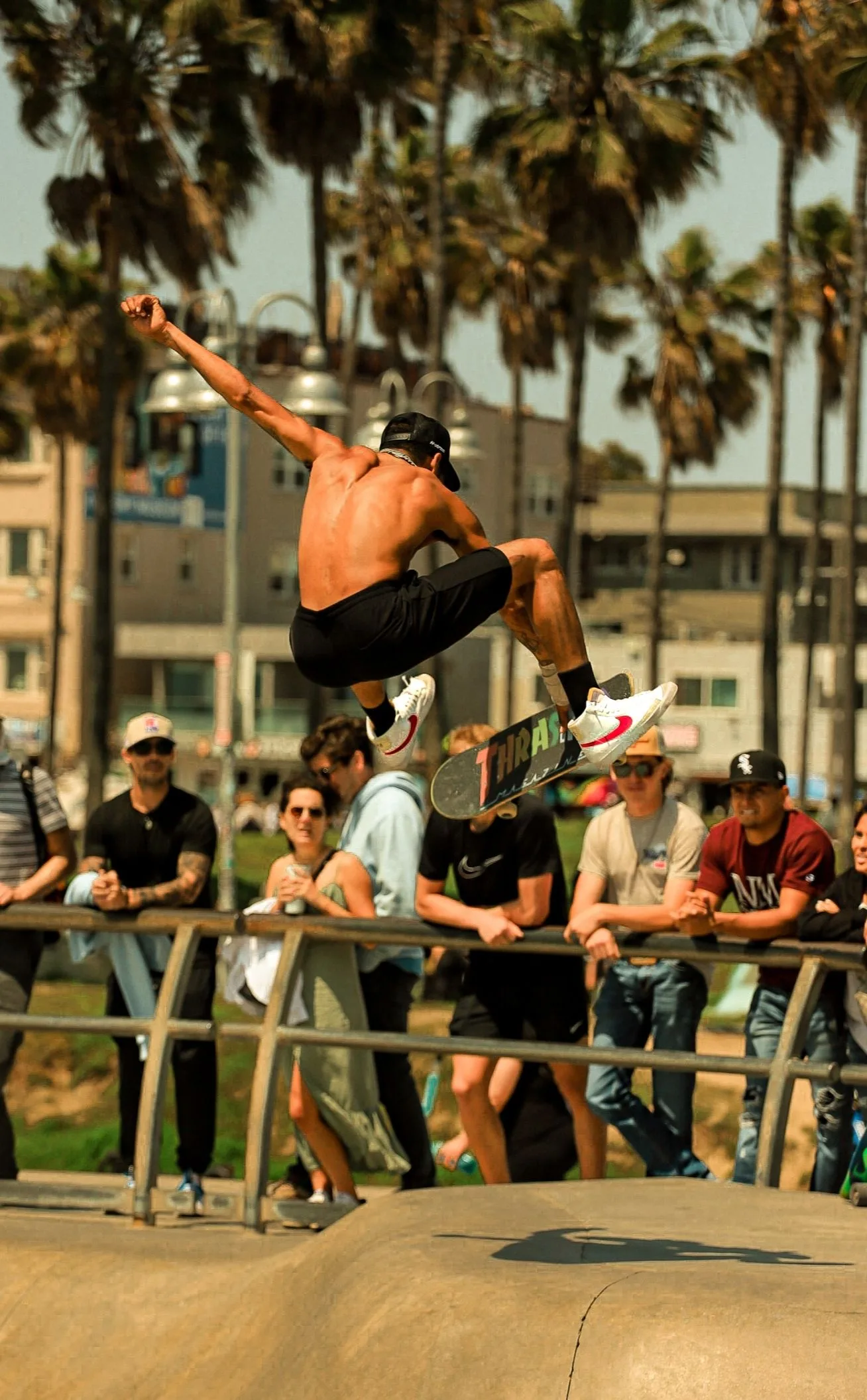 Skateur en pleine figure au-dessus d’un bowl, palmiers en arrière-plan