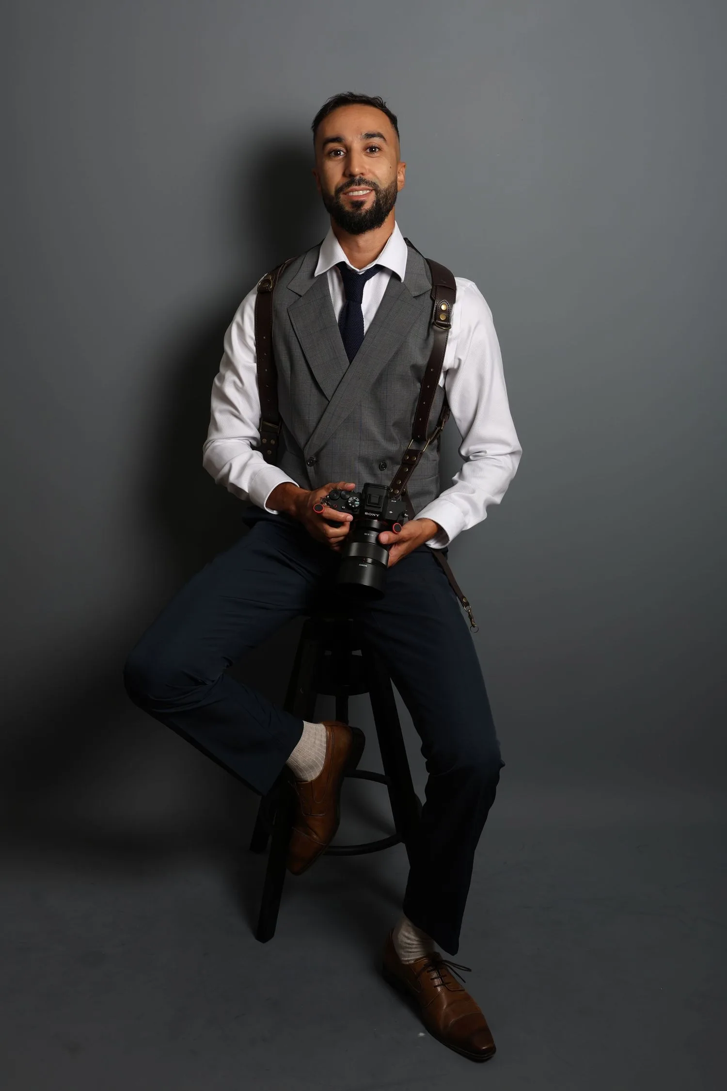 Malik Rahmouni en gilet gris, son appareil photo à la main, en studio