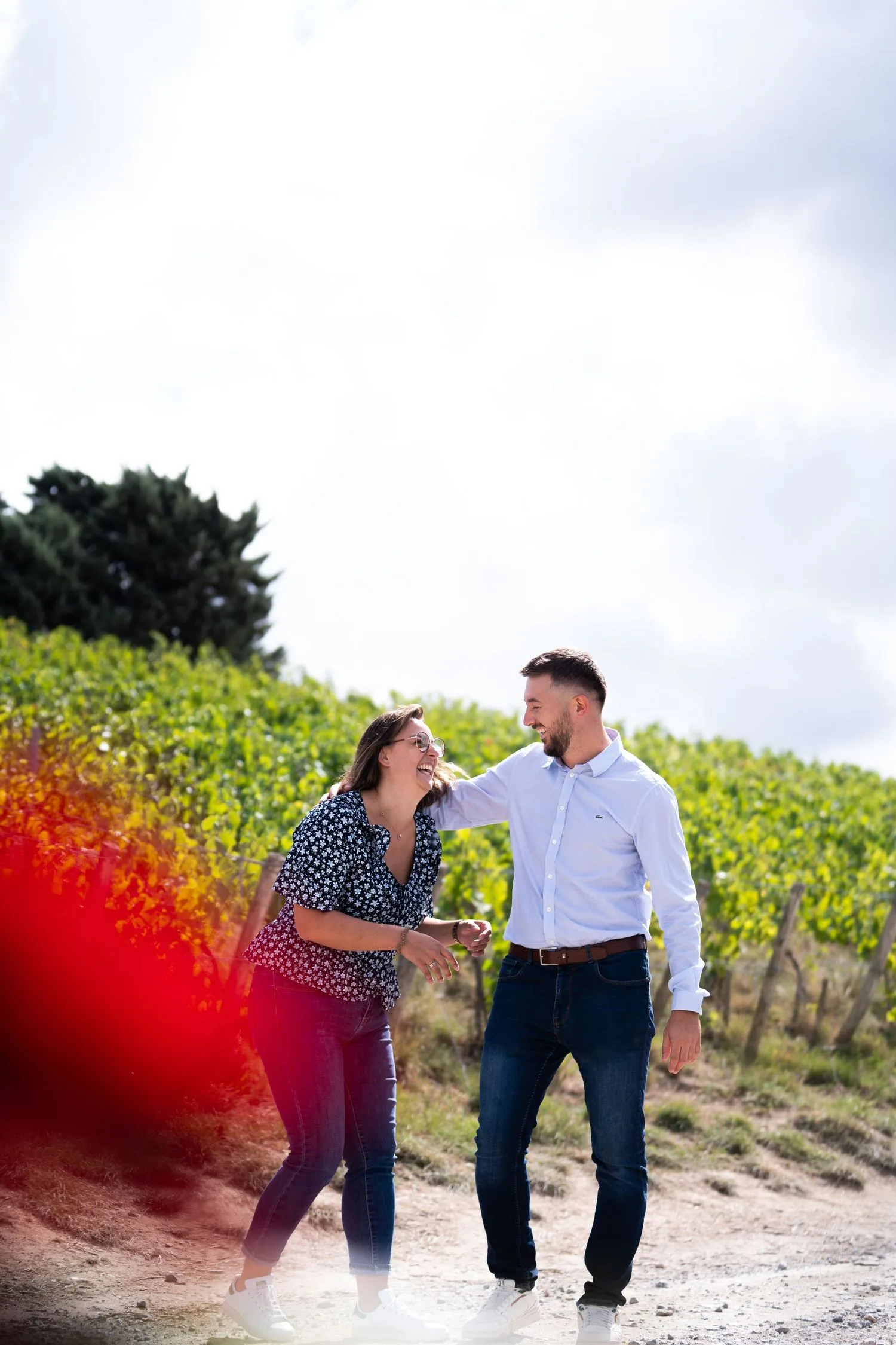 Un couple rit en marchant sur un chemin bordé de vignes lors d’une séance photo