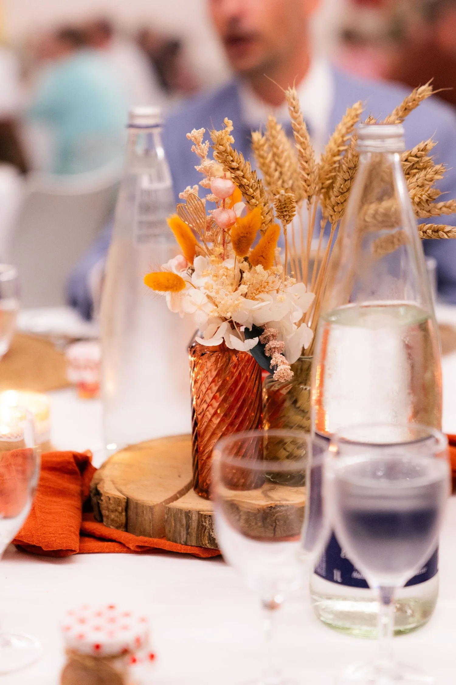 Centre de table en fleurs séchées dans un vase ambré posé sur une rondelle de bois