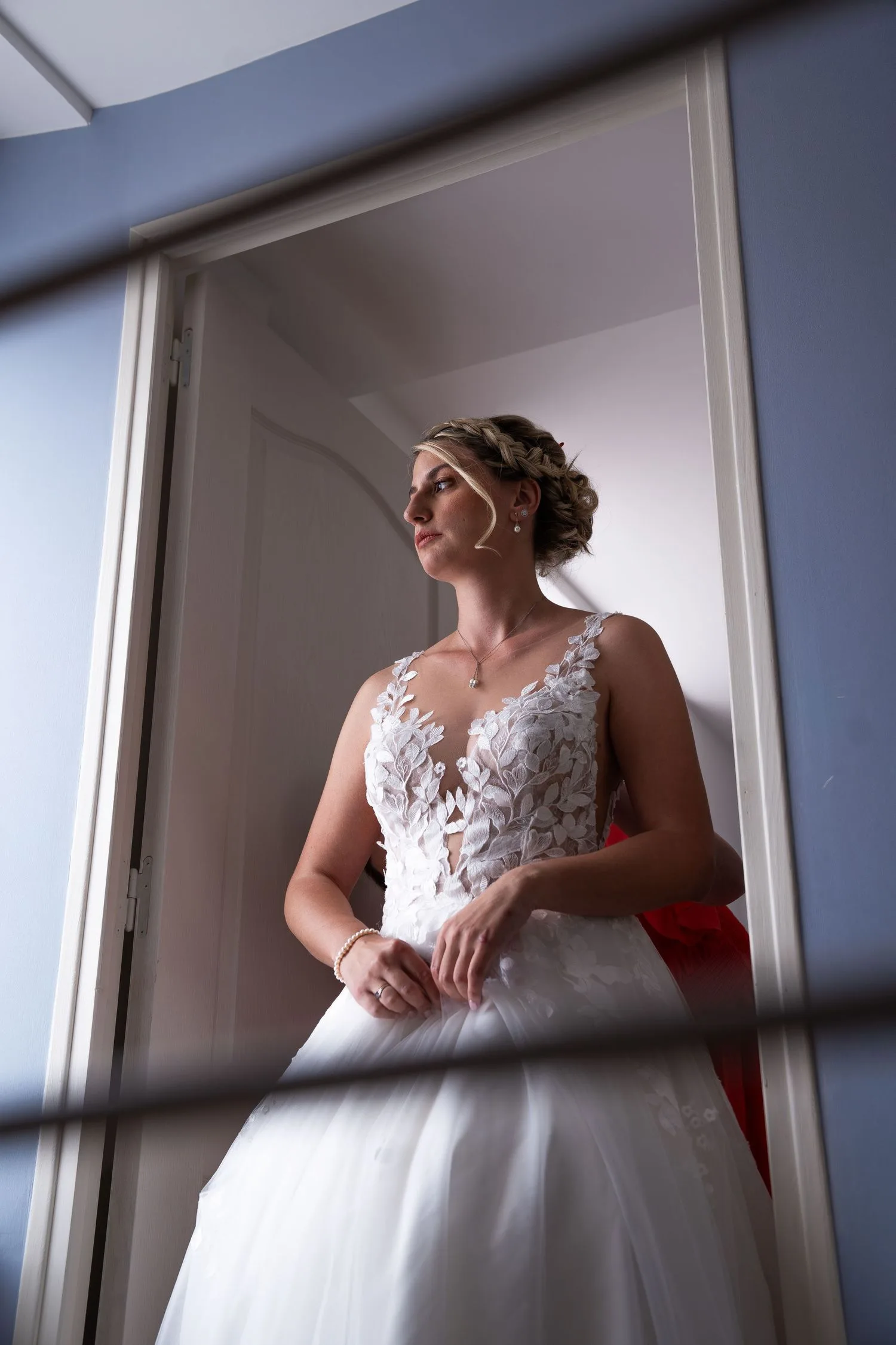 La mariée seule dans l’embrasure d’une porte, couronne de tresses et robe en dentelle