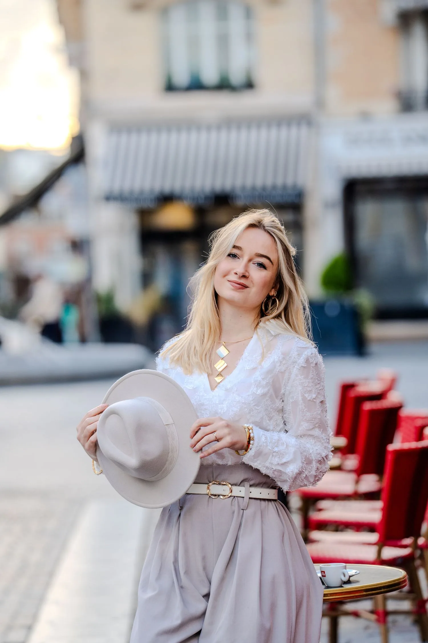 Portrait en ville : jeune femme tenant un chapeau en feutre, terrasse aux chaises rouges