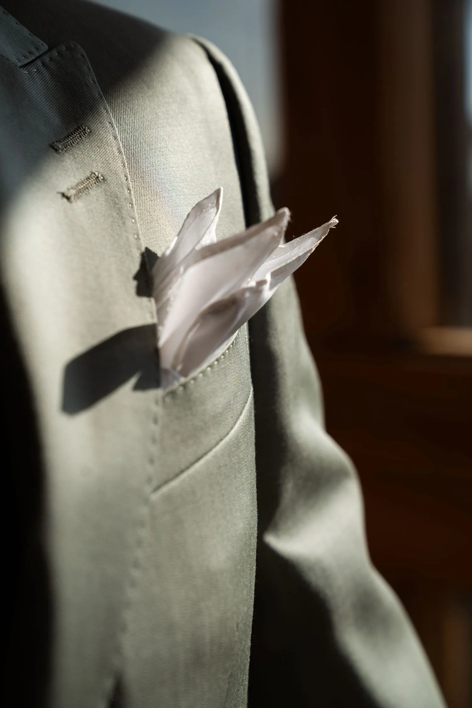 Détail d’une veste de costume vert sauge et de sa pochette en soie rose poudré