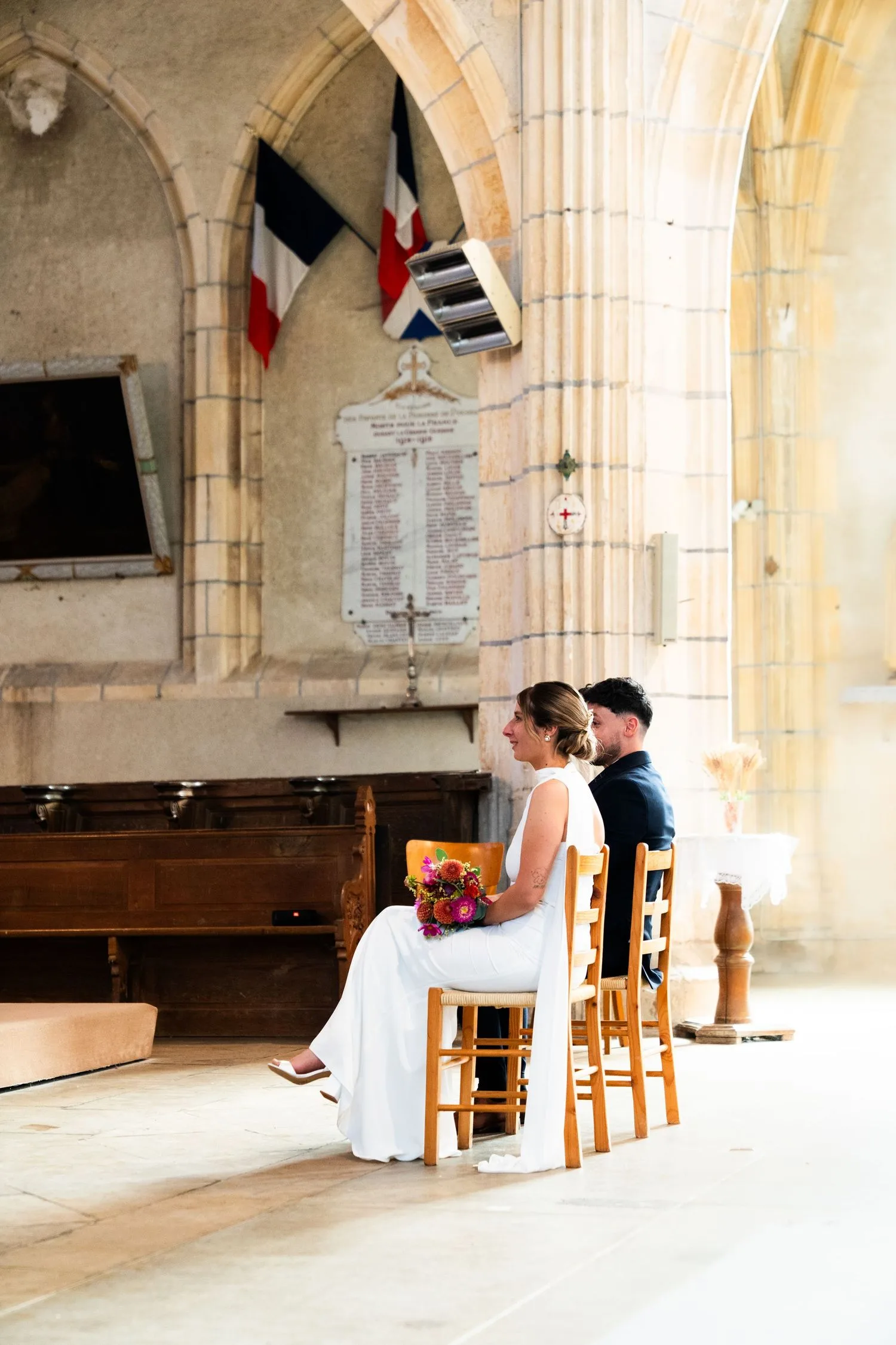 Les mariés assis pendant la cérémonie, sous les arches de pierre de l’église