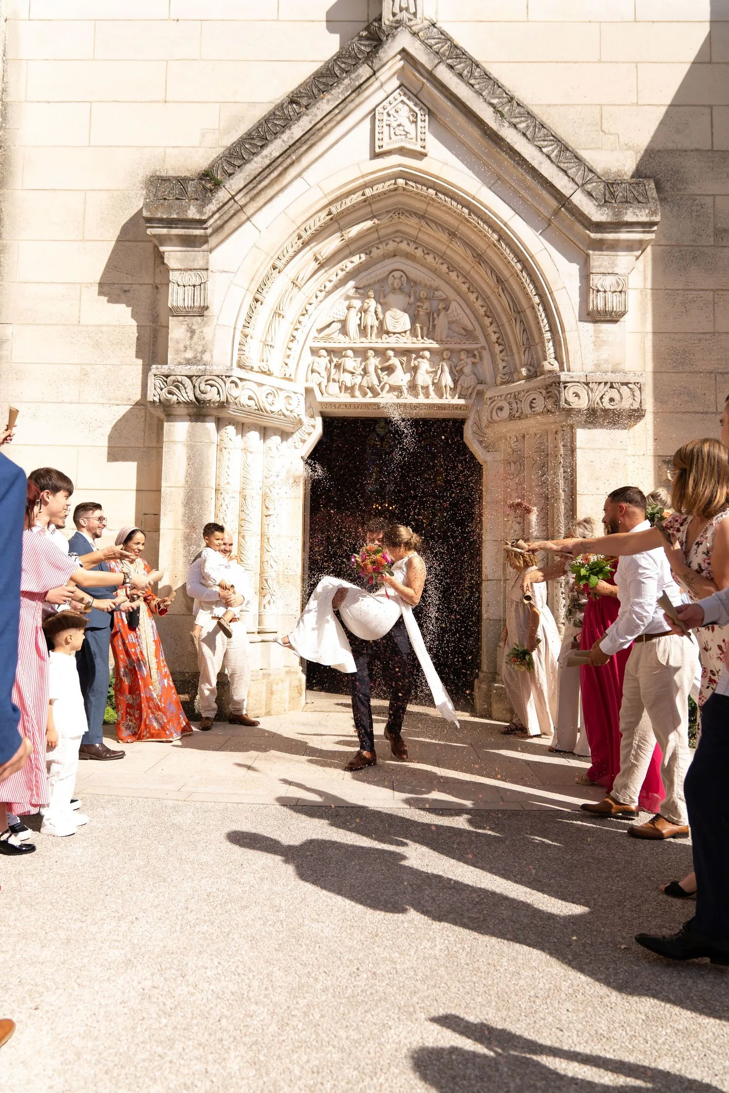 Sortie d’église sous une pluie de confettis, le marié portant la mariée dans ses bras