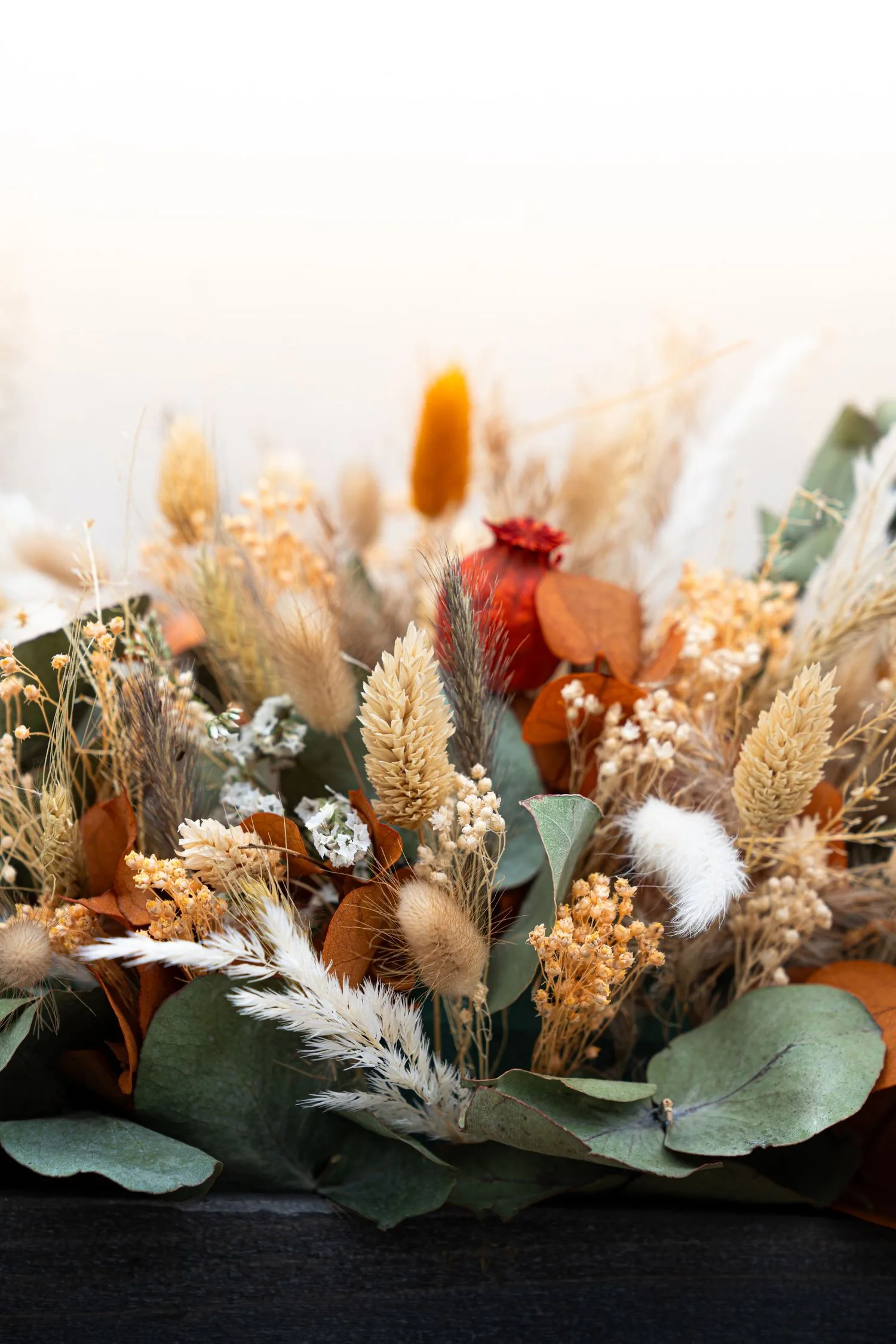 Gros plan d’un bouquet de fleurs séchées : blé, eucalyptus et feuillage terracotta
