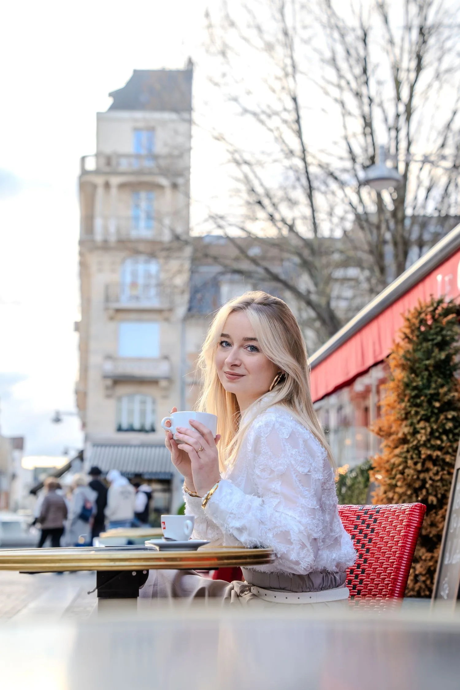 Portrait en terrasse : tasse de café à la main devant une façade en pierre