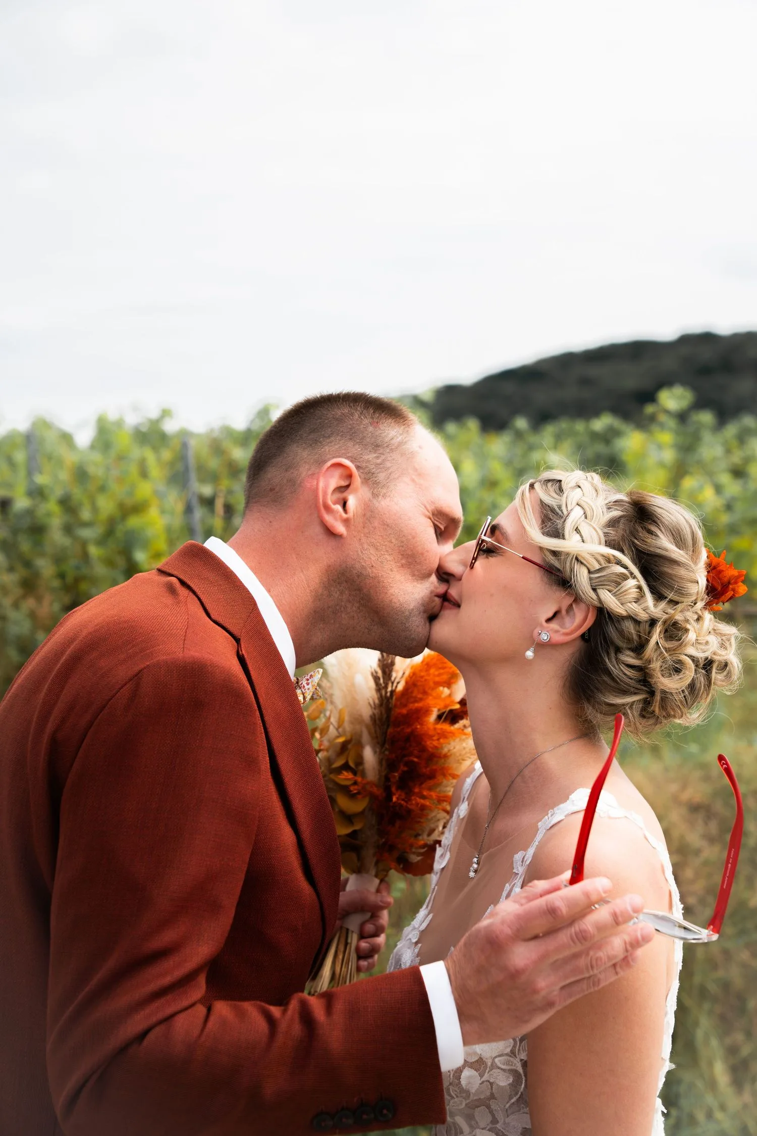 Les mariés s’embrassent dans les vignes, la mariée coiffée d’une couronne de tresses