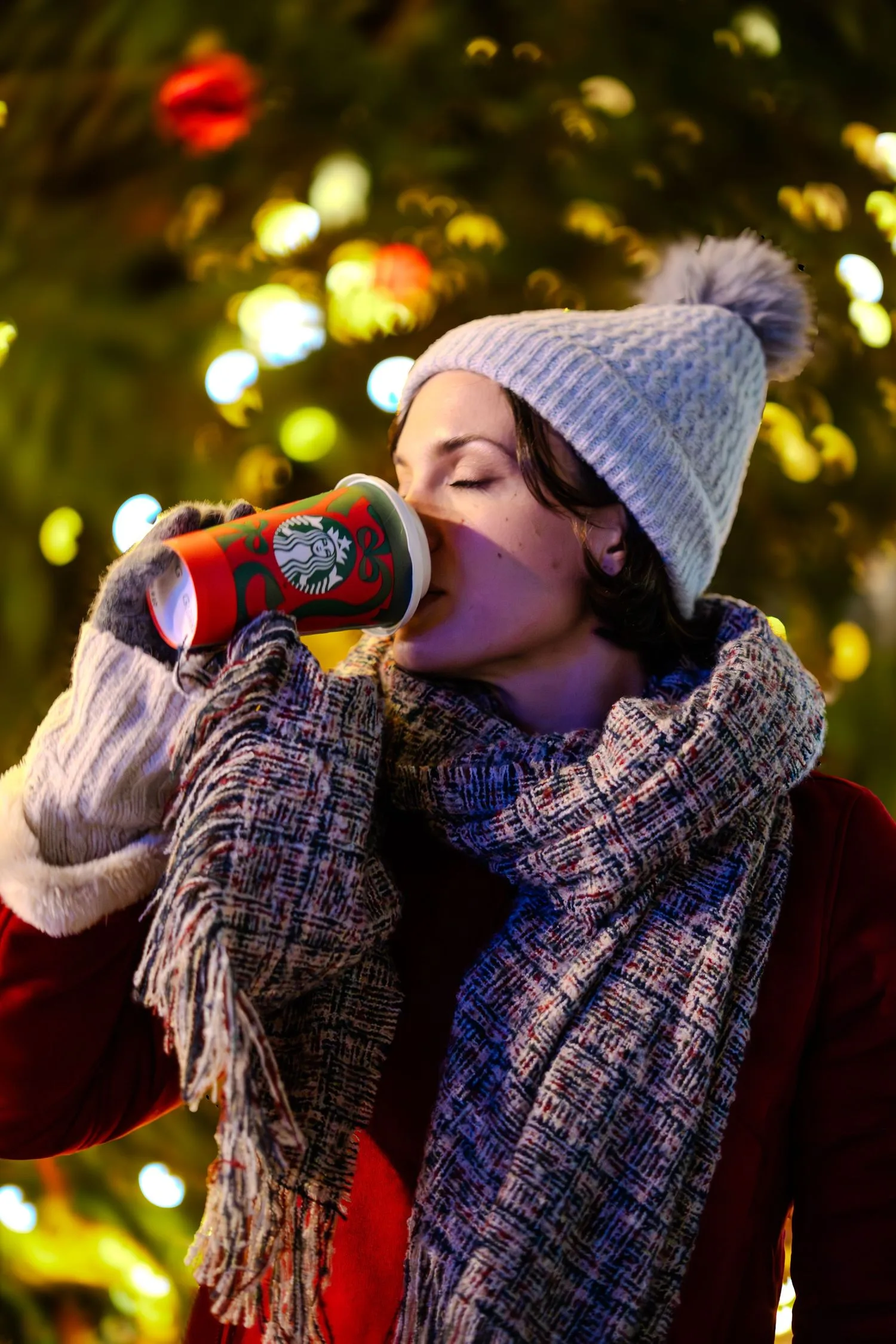 Portrait d’hiver : boisson chaude à la main devant un sapin illuminé, bonnet et écharpe