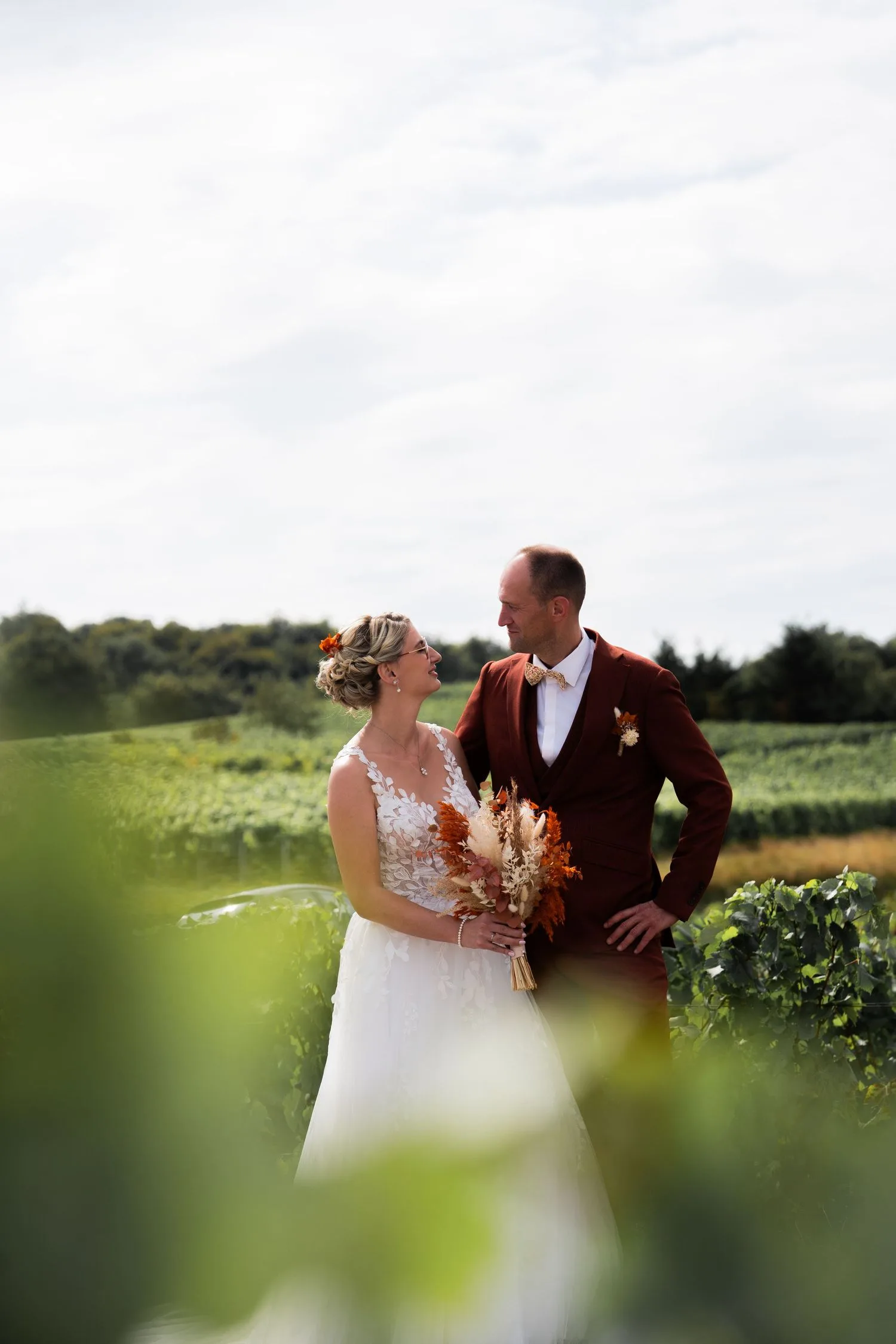 Les mariés dans les vignes, costume bordeaux et nœud papillon doré