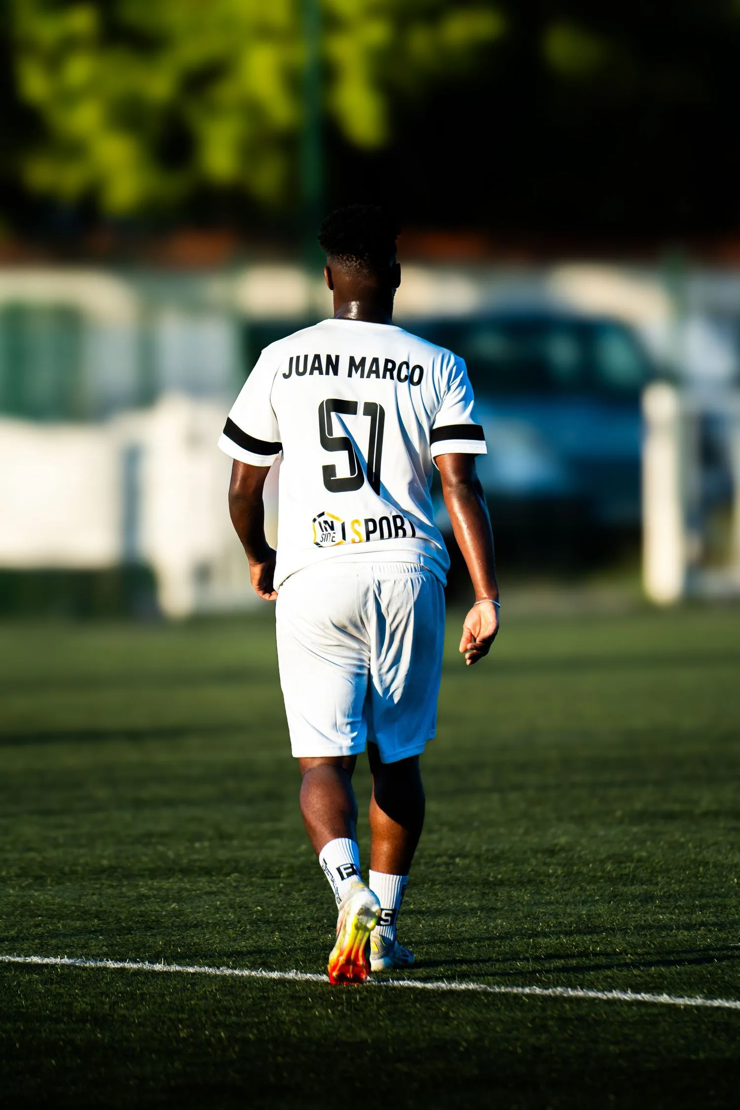 Un footballeur de dos marche sur la pelouse, maillot blanc floqué numéro 51