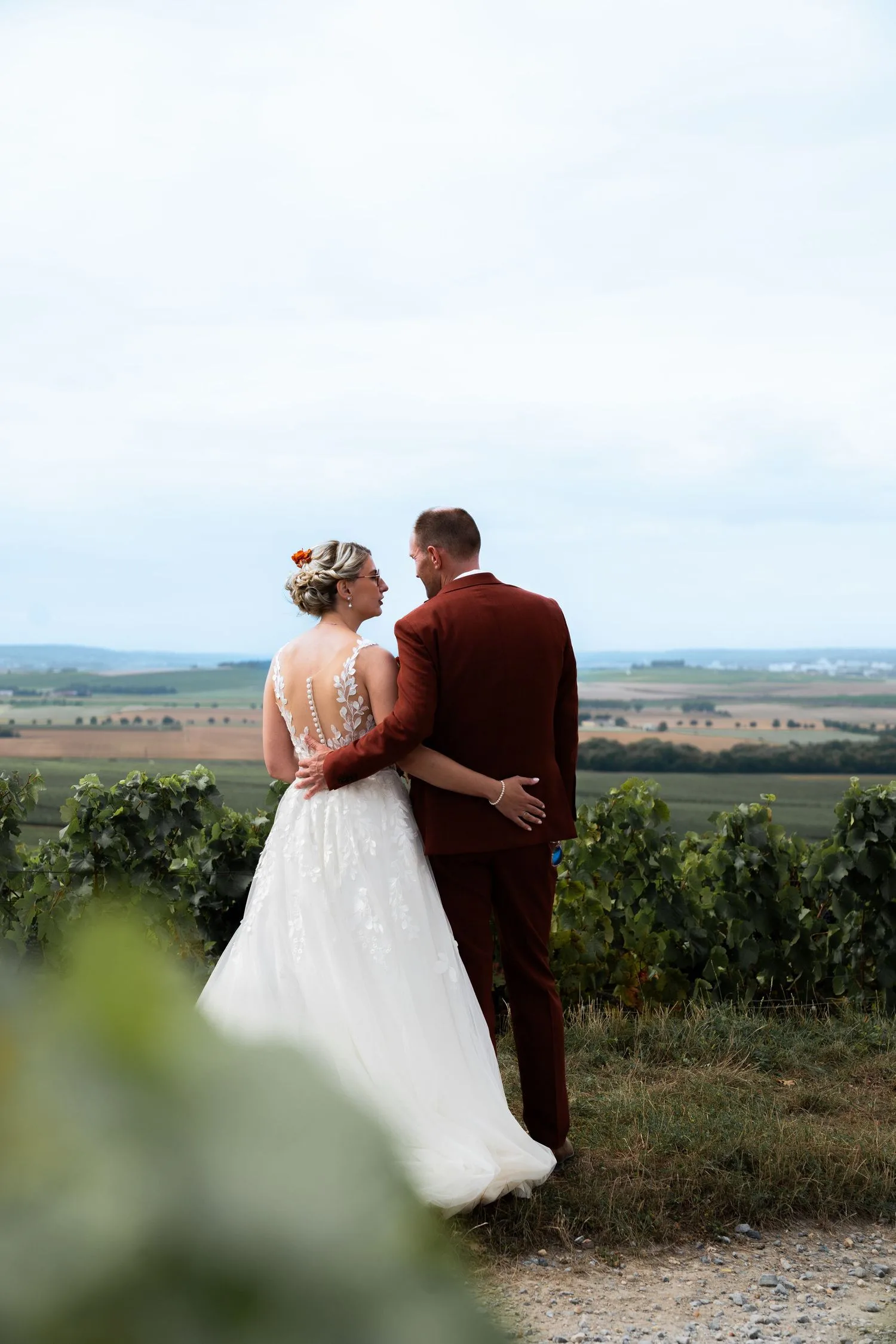 Les mariés de dos contemplent les vignes et la plaine à l’horizon