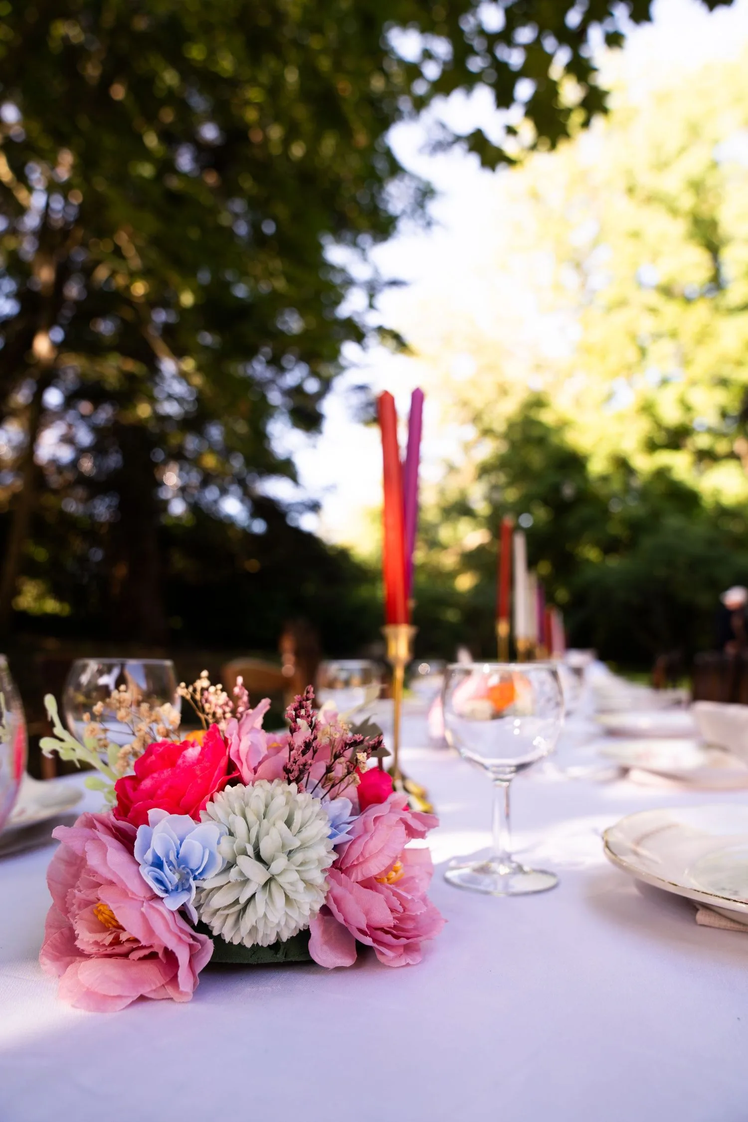 Table de réception dressée en plein air sous les arbres, fleurs roses et bougies rouges
